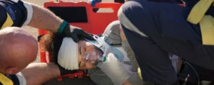 Emergency medical responders in reflective vests are treating an injured patient with an oxygen mask on a red stretcher, representing pain and suffering from accident injuries.