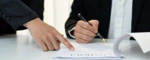A man in a black suit is signing a legal settlement document with a pen, representing an emotional distress settlement value agreement.