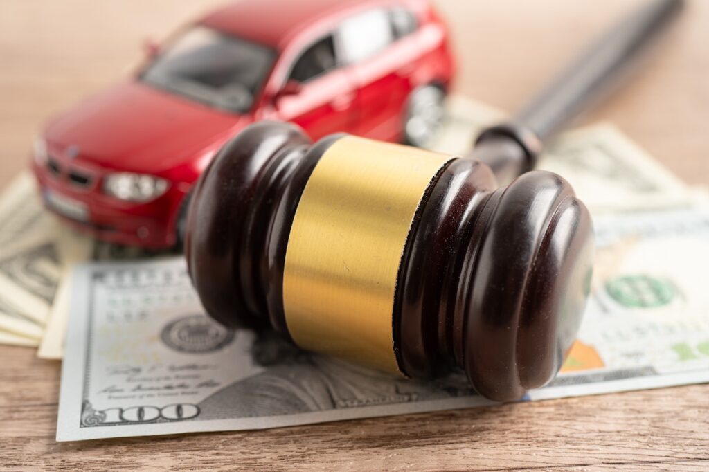 A wooden gavel with a gold band resting on a dollar bill with a red toy car and a calculator in the background, representing maximum compensation from an accident settlement.