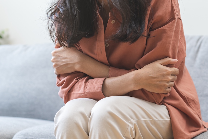 A woman sitting alone on a couch hugging herself with her arms wrapped tightly around her body depicting the emotional trauma and PTSD experienced by car accident survivors in Atlanta.