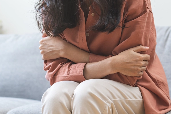 A woman sitting alone on a couch hugging herself with her arms wrapped tightly around her body depicting the emotional trauma and PTSD experienced by car accident survivors in Atlanta.