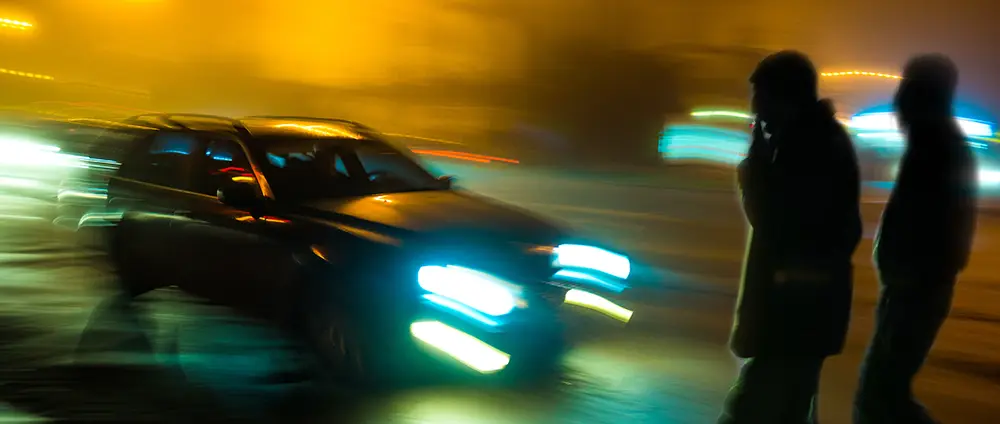 A pedestrian walking at night while a car is speeding towards them representing an accident a pedestrian accident lawyer would review.