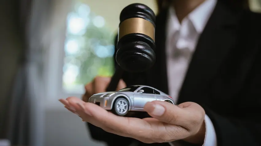 A woman in a suit is holding a judge's gavel over a small model car symbolizing the legal process involved in pursuing a car accident injury claim at Amircani Law in Atlanta.