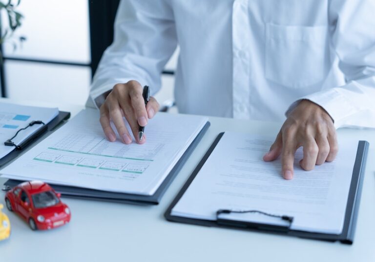 A person in a white dress shirt reviews two documents side by side on a desk with a pen in hand and a small red toy car nearby depicting the careful line-by-line review an attorney from Amircani Law conducts before advising a client to accept or reject a first settlement offer in Metro Atlanta.