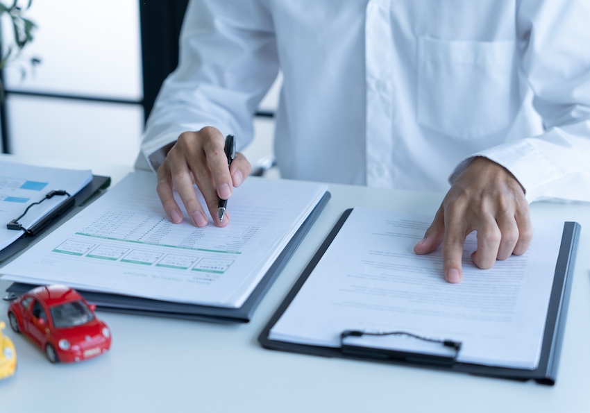 A person in a white dress shirt reviews two documents side by side on a desk with a pen in hand and a small red toy car nearby depicting the careful line-by-line review an attorney from Amircani Law conducts before advising a client to accept or reject a first settlement offer in Metro Atlanta.