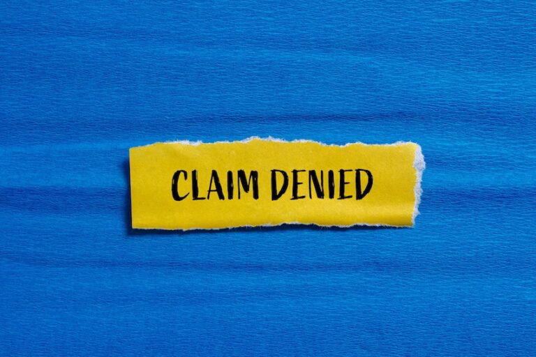 A torn yellow paper strip with the words "Claim Denied" printed in bold black letters against a blue background- representing the frustrating outcome an accident victim faces when a driver's insurance company refuses to pay out a legitimate injury claim in Metro Atlanta with help from Amircani Law.