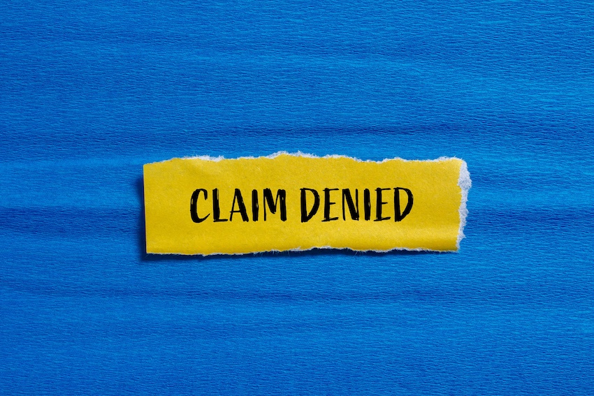 A torn yellow paper strip with the words "Claim Denied" printed in bold black letters against a blue background- representing the frustrating outcome an accident victim faces when a driver's insurance company refuses to pay out a legitimate injury claim in Metro Atlanta with help from Amircani Law.