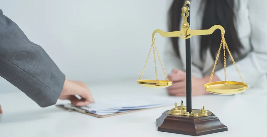 An attorney from Amircani Law and a client are sitting beside a gold scale of justice, representing the legal consultation process that often follows when a victim disputes a settlement offer from a driver's insurance company after a collision.